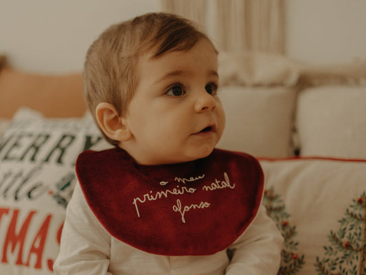 Bebé com um babete de veludo vermelho com a frase o meu primeiro natal